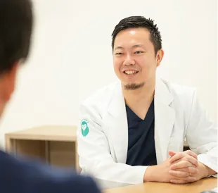 診察室で白衣を着た医師が相談者と向かい合い、穏やかに話を聞いている様子